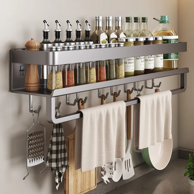 A black aluminum wall mounted kitchen shelf installed on a kitchen wall, holding spice jars and hanging utensils.