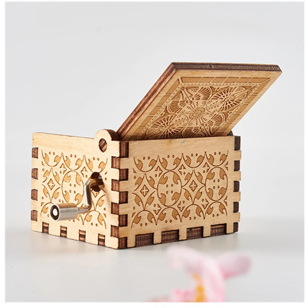 A petite, intricately crafted wooden music box with detailed laser-engraved patterns sits slightly ajar, showcasing its elegant winding key on the side. These handmade Wooden Music Boxes are ideal for playing timeless melodies and infuse any space with vintage charm.