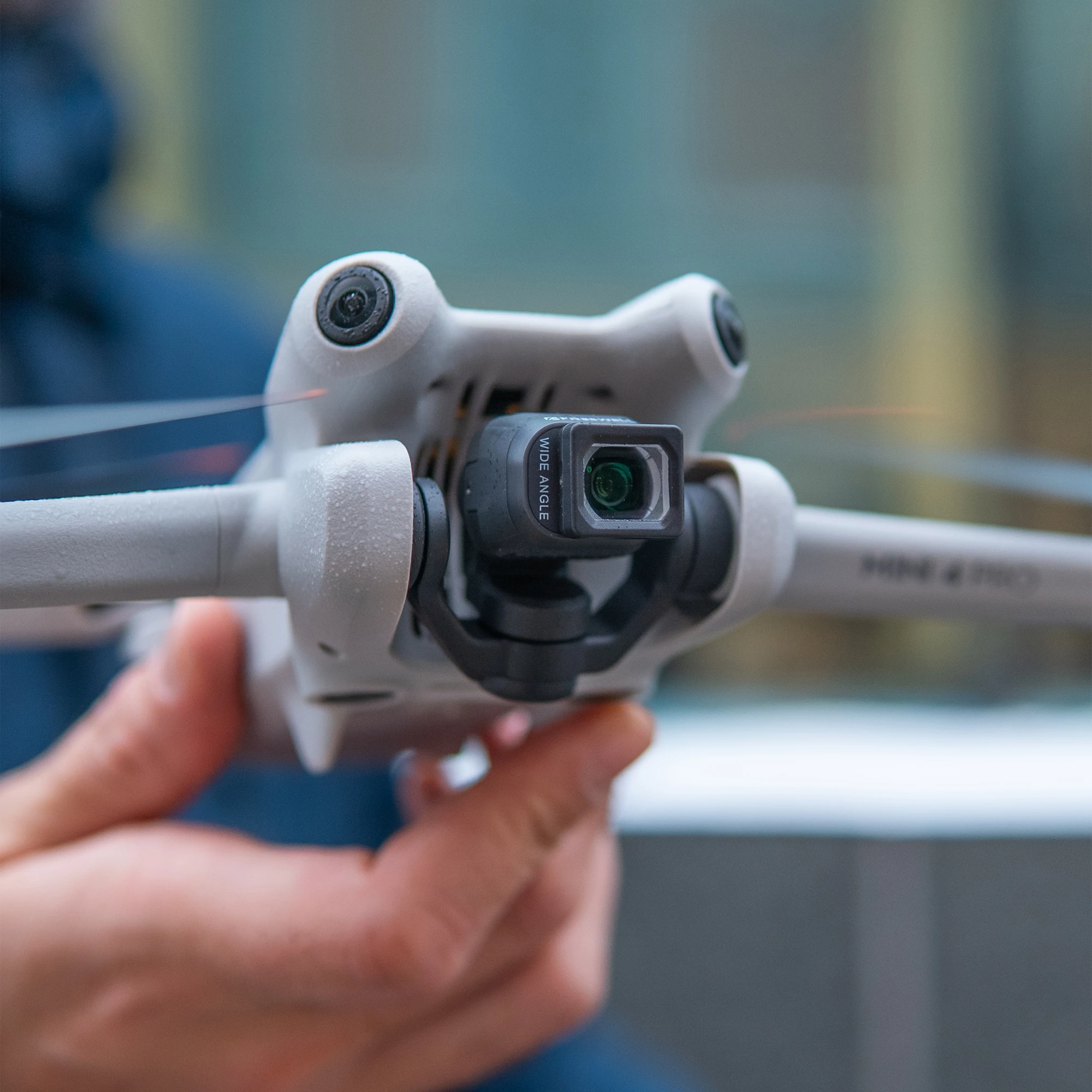 Drone DJI Mini 4 Pro équipé du Kit Objectif Grand Angle et Anamorphique FrePS en vol, paysage urbain en arrière-plan.