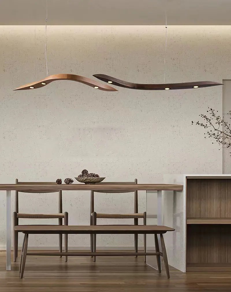 Minimalist dining area with a wooden table, two benches, décor, and the Spiral Wood Pendant Light casting warm light from above against a textured wall, with a plant in the corner.